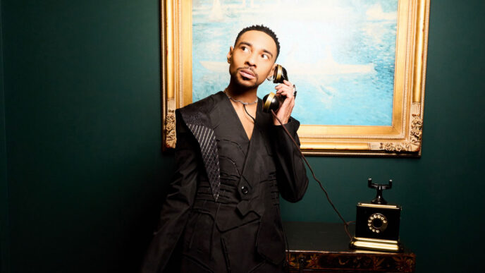 Man in a black suit holding vintage telephone to his ear in a dark, artful room with a gold-framed seascape painting behind him.