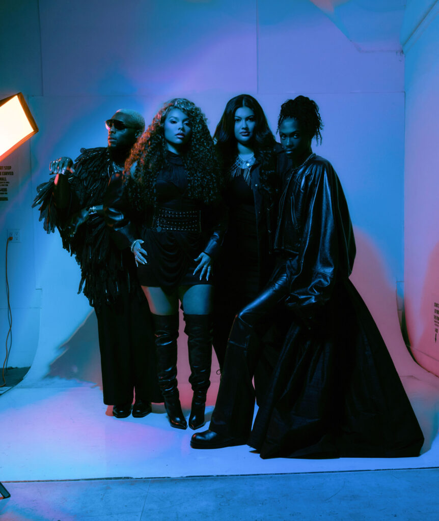 - Groovevolt Four models pose together in a photography studio with blue and purple lighting; they wear dark, dramatic outfits and tall boots for a fashion shoot.