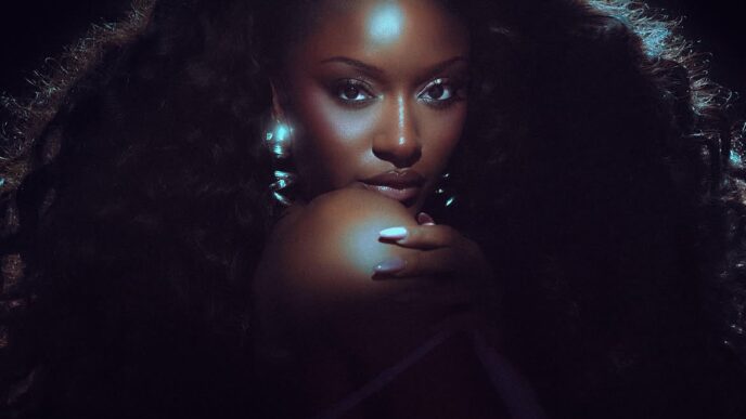 Glamour portrait of a woman with voluminous curly hair and blue backlighting, hand resting near her chin, looking at the camera.