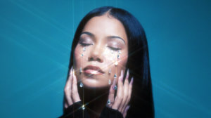 Woman with eyes closed, crystal teardrops on her face against a teal background, artistic makeup look