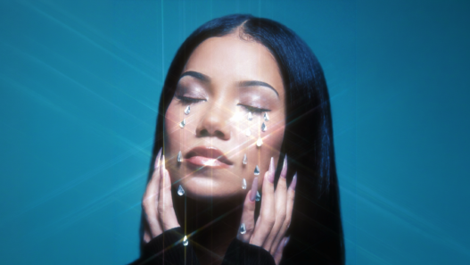 Woman with eyes closed, crystal teardrops on her face against a teal background, artistic makeup look