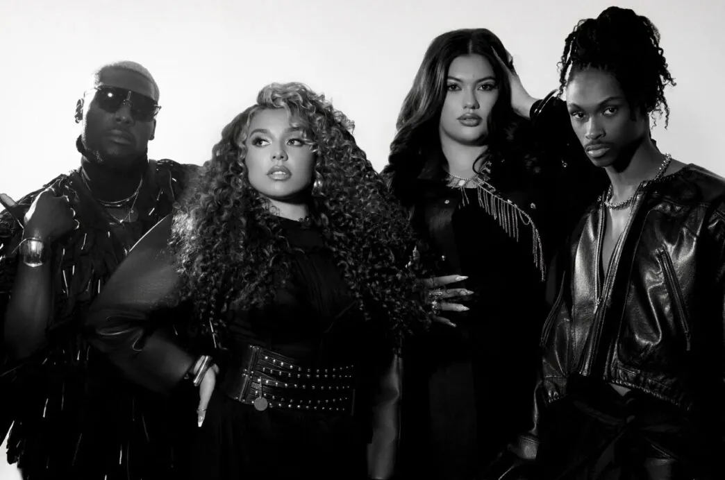 Group of four fashion-forward individuals posing together in studio wearing all-black outfits.