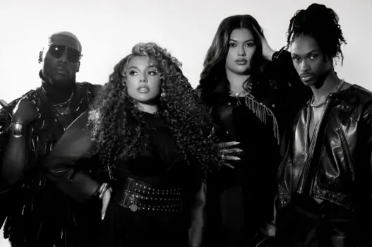 Group of four fashion-forward individuals posing together in studio wearing all-black outfits.