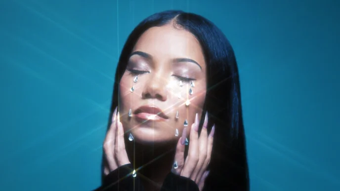 Woman with eyes closed, crystal teardrops on her face against a teal background, artistic makeup look