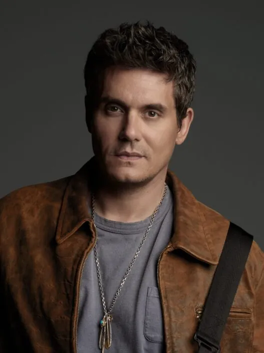 Portrait of a man with short dark hair wearing a brown leather jacket and gray tee, against a dark backdrop.